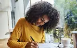 Vrouw Met Gele Trui Schrijft Op Tafel